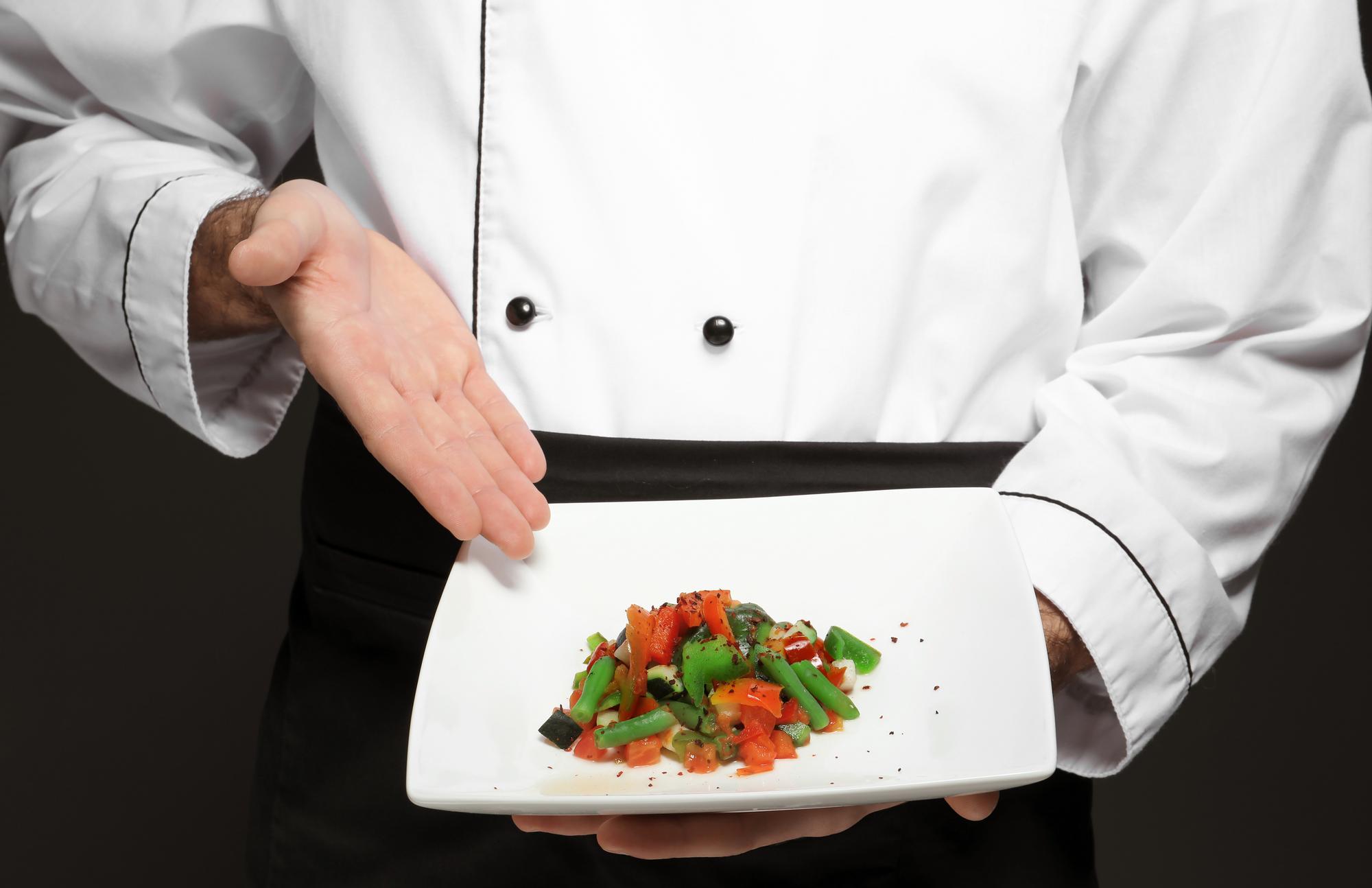 Chef presenting plated dish on dark table